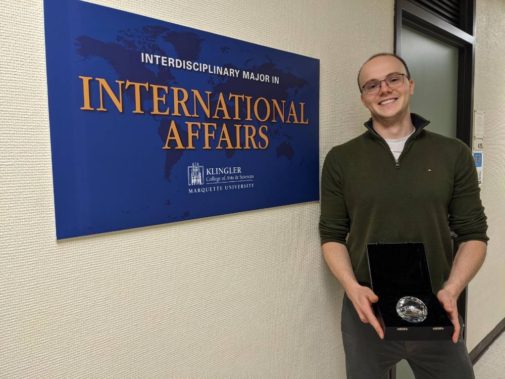 William Goltra, the 2022-2023 INIA Scholar of the Year Award recipient holding the award and standing next to the International Affairs sign.