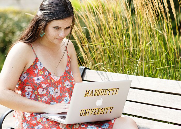 Student outdoors using laptop with Marquette University decal