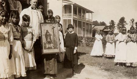 Choctaw Indian children holding a poster of St. Kateri Tekakwitha and joined by a priest of the Missionary Servants of the Most Holy Trinity and a sister of the Missionary Servants of the Blessed Trinity at Holy Rosary Mission, Tucker, Mississippi, 1934