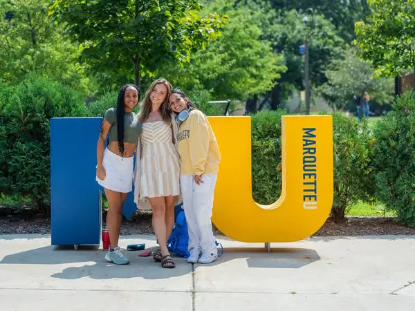 three marquette students in front of award winning instalation of MU letters in front of memorial union