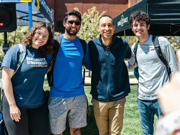 Three students getting a picture with Marquette basketball coach Shaka Smart