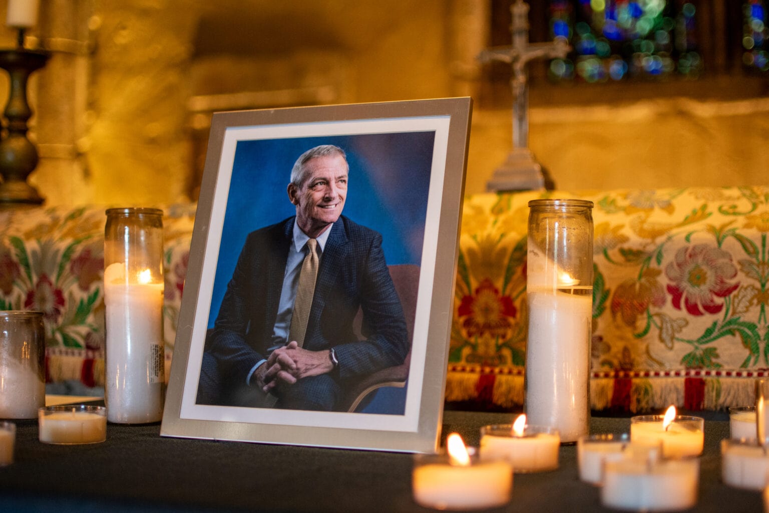 A potrait of President Lovell in a frame on a desk, surrounded by lit candles.