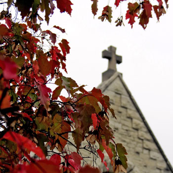 The cross on top of St. Joan of Arc Chapel framed by fall leaves
